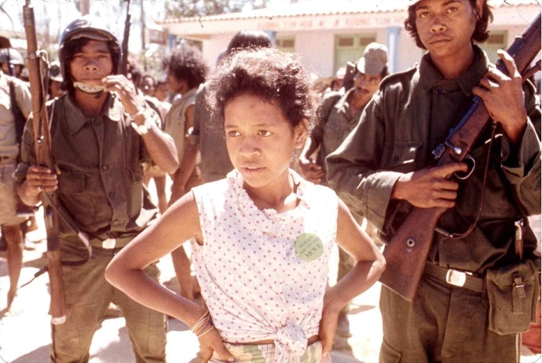 Elemen sipil dan bersenjata selama kudeta UDT di bulan Agustus 1975, nampak seorang perempuan dengan tulisan di dada berbunyi: ""Women are on the move.'[Archives & Museum of East Timorese Resistance]